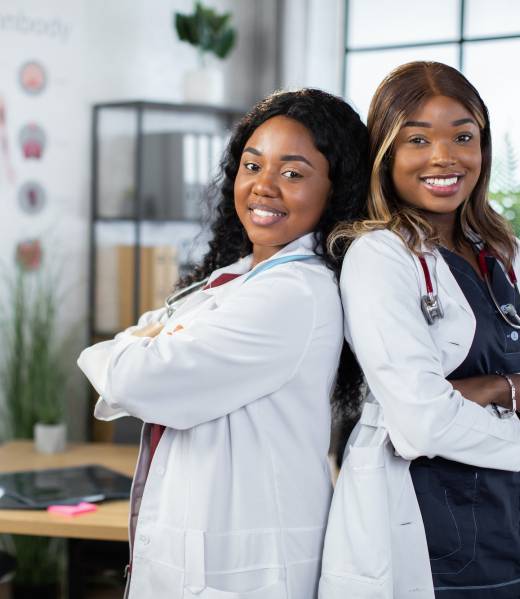 Two beautiful young female black skinned african doctors, standing back to back with arms crossed